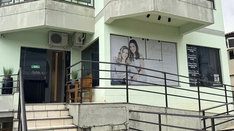 Fachada da Clínica Revitalize, prédio claro com escada e o painel da equipe na vitrine