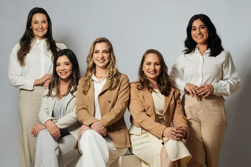 As cinco profissionais da equipe Revitalize, de roupas claras, sorrindo juntas